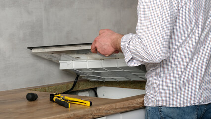 A young repairman installs a black induction hob in a modern white Scandinavian style kitchen with...