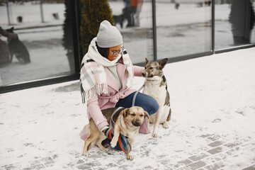 Cute african girl in a winter park. Woman in a pink coat. Lady with a two dogs.