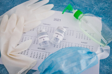 covid-19 vaccine against the pandemic, ampoules with Vaccine 1 and Vaccine 2 labels side by side next to 2021 yearly calendar  and gloves mask and sanitizer