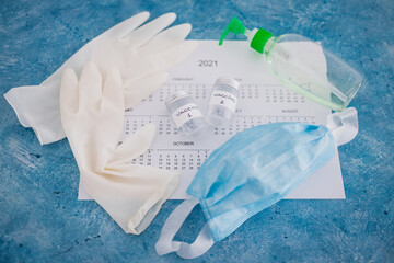 covid-19 vaccine against the pandemic, ampoules with Vaccine 1 and Vaccine 2 labels side by side next to 2021 yearly calendar  and gloves mask and sanitizer
