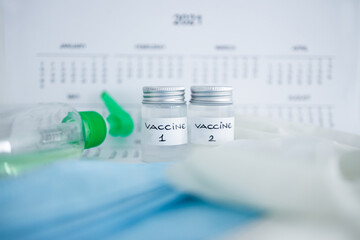 covid-19 vaccine against the pandemic, ampoules with Vaccine 1 and Vaccine 2 labels side by side next to 2021 yearly calendar and mask gloves and sanitizer