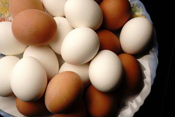A lot of white and brown chicken eggs are on the plate. Top view.