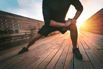 Sporty man stretching leg adductor muscles and warming up for training outdoors at sunset or...