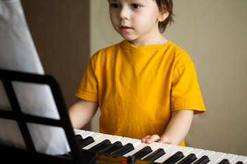 A boy playing the synthesizer. Toddler learning how to play piano. Child's hands on the keyboard. Early development and education concept