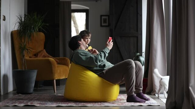 father and son looking at the phone screen while sitting in a  beanbag chair at home