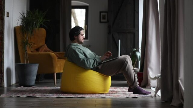 man working on outsource with laptop and playing with dog in same time at home