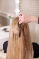 Fototapeta premium Hairdresser's hand brushing long natural blonde hair in beauty salon