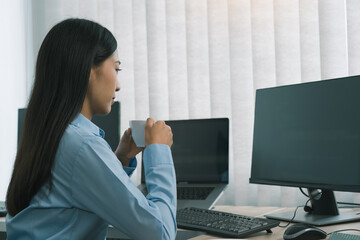Asian woman was drinking coffee in the early morning while contemplating the program and code on the computer screen.