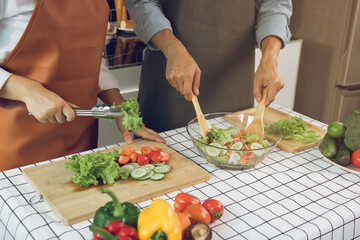 Asian couple enjoying cooking vegetable salad in the kitchen.