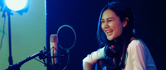 A cute Asian singer and musician playing guitar and sing a song for recording in voice studio.