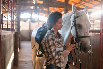 Portrait of female farmer standing with white horse at stabling indoor