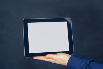 Businessman in a blue jacket holds a mock-up of a tablet with a white screen on a dark background.