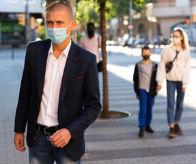 Man in protective face mask for spreading of virus disease prevention walking on city street. High quality photo