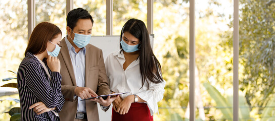 Fototapeta na wymiar coronavirus prevention in the office. Group of Asian business people wearing face masks standing reading working discussion in a meeting room. Covid-19 new normal lifestyle concept