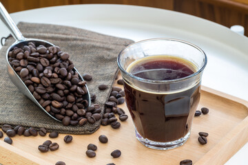Hot Espresso in glass place near coffee bean pile. International famous aroma beverage. Cup of coffee on an old wooden table.