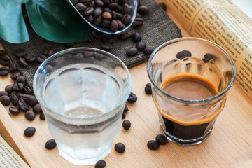 Espresso shot in glass place near coffee bean pile. International famous aroma beverage. Cup of coffee on an old wooden table.