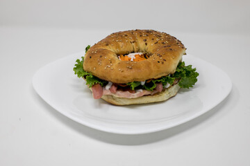 Primer plano de un sándwich de rosquilla tostada con lechuga fresca y jamón en un plato blanco