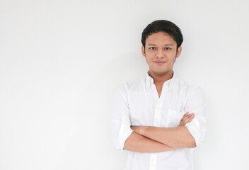 Young Asian man wearing white shirt is holding hands crossed with happy smile and confidence. Successful Indonesian man on gray background.