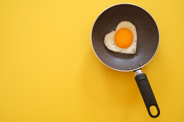 Heart shape fried egg in the pan on yellow background. top view. healthy food  concept.  Copy space for text 