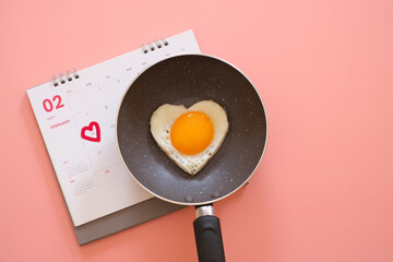 Heart shape fried egg in the pan on the calendar with valentine day marked isolated on pink background. top view. Valentine's day concept.  Copy space for text 