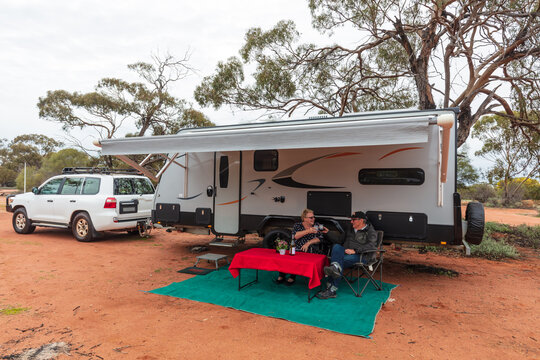 Retired Australian senior citizens known as "Grey Nomad" relax with a glass of wine outside of their modern caravan camped in the outback.