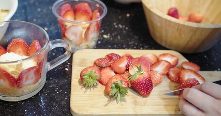 Person using knife cutting group of fresh red strawberry on wooden cutting board
