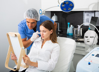 Obraz premium Professional male cosmetician consulting young woman before facial treatment in cosmetological office.