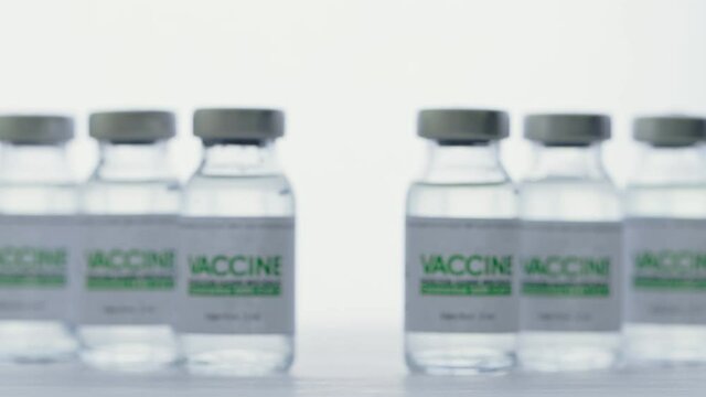 Doctor with glove takes flask of vaccine for injection for coronavirus COVID-19 cure in research laboratory. Vaccination concept, pandemic. Macro. Bottles, vials, flacons are on white light background
