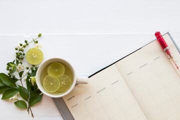 notebook planner for business work and mix honey lemon herbal hot healthy drinks for sore throat with lemon slice and white flower jasmine arrangement flat lay style on background white wooden