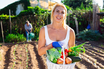 Satisfied young woman engaged in cultivation of organic vegetables in her small garden showing good harvest