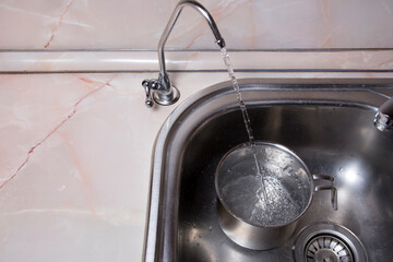 Pouring filtered water into pot from water filter. Closeup of sink and faucet. Drinkable water in kitchen