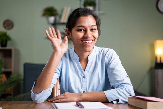 Young business woman saying hai gesture or waving hands to camera - Concept of video chat, conference or vlogging from home by looking at camera.