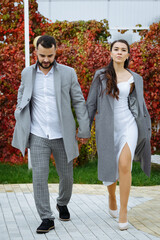 Stylish couple in gray coats walking in the autumn park. Happy sensual wedding couple. Romantic moments of newlyweds.
