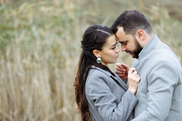 Stylish couple in gray coats gently hugging on the background of reeds. Happy sensual wedding couple embracing. Romantic moments of newlyweds.