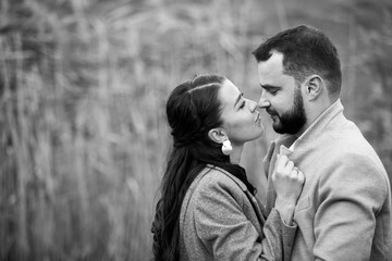 Fototapeta premium Stylish couple in gray coats gently hugging on the background of reeds. Happy sensual wedding couple embracing. Romantic moments of newlyweds.