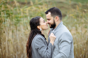 Stylish couple in gray coats gently hugging on the background of reeds. Happy sensual wedding couple embracing. Romantic moments of newlyweds.