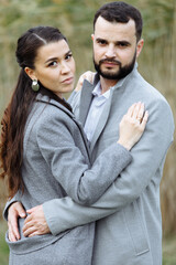 Stylish couple in gray coats gently hugging on the background of reeds. Happy sensual wedding couple embracing. Romantic moments of newlyweds.