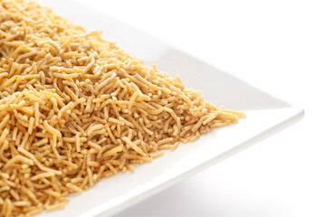 Salty plane Bhujia in a white ceramic square plate, made with Chickpeas or gram flour (Besan). Pile of Indian salty snacks (Namkeen), under backlight, side view