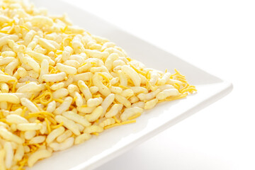 Crunchy Lemon Bhel in a white ceramic square plate made with Puffed Rice small besan sev. Pile of Indian spicy snacks (Namkeen)  under backlight side view 