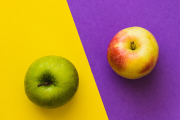 Green apple and yellow-red apple, on a half purple and half yellow background