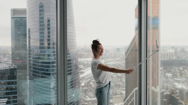 Attractive girl tourist taking selfie near window in modern hotel with city view from high floor