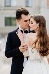 beautiful, gentle and happy bride and groom hugging on background of building