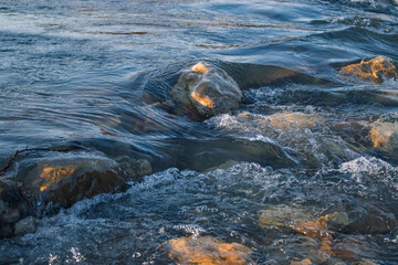 Bubbling water stream of a mountain river with splashes of large stones of a rocky channel on a sunny day.