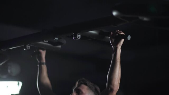Athletic man performs pull-ups on the horizontal bar, strength training in the gym, cinematic light.