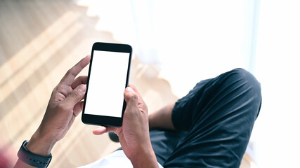 Close up view of young man sitting  with crossed legs in living room and using smart phone.