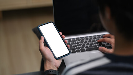 Rear view of young man freelancer working with laptop computer and using mobile phone at home.