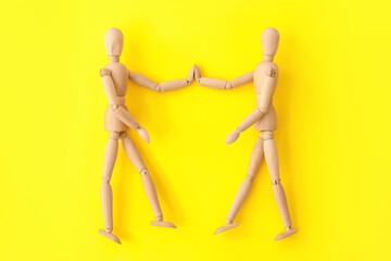 Wooden mannequins holding hands on color background