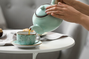 Woman pouring tea from teapot into cup on table in room