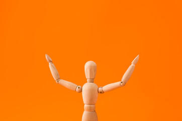 Wooden mannequin raising hands on color background
