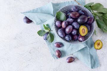 Bowl with tasty plums on light background